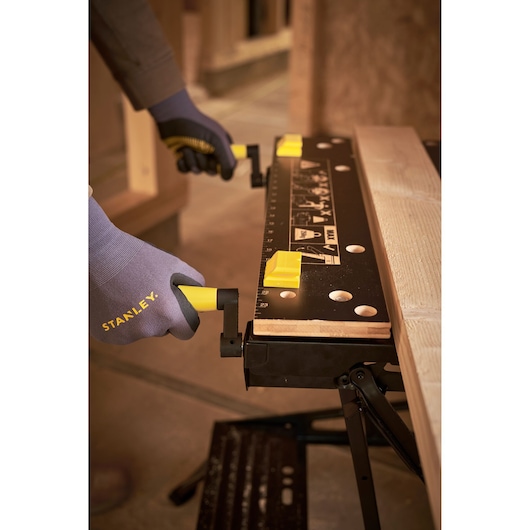 STANLEY STST83400-1 workbench with black top and yellow clamps, close-up of hands adjusting handles.