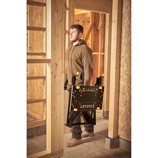 Photo of STANLEY STST83400-1 workbench being carried, folded, in a construction site.