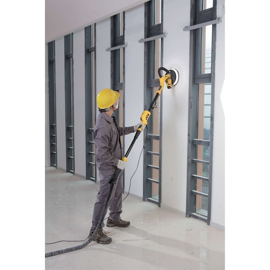 Stanley SW75-BR drywall sander in use by worker with yellow hard hat, sanding an interior wall.