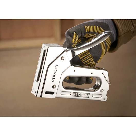 Photo of STANLEY TR110 heavy duty stapler held in gloved hand, chrome finish, close-up view.