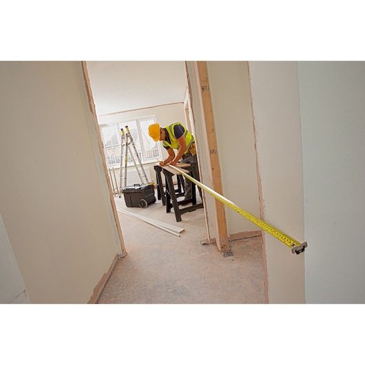 STANLEY XTHT0-33504 tape measure in use by worker measuring across doorway on construction site.