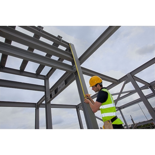 STANLEY XTHT0-33504 tape measure in use by worker measuring steel frame at construction site, side angle.